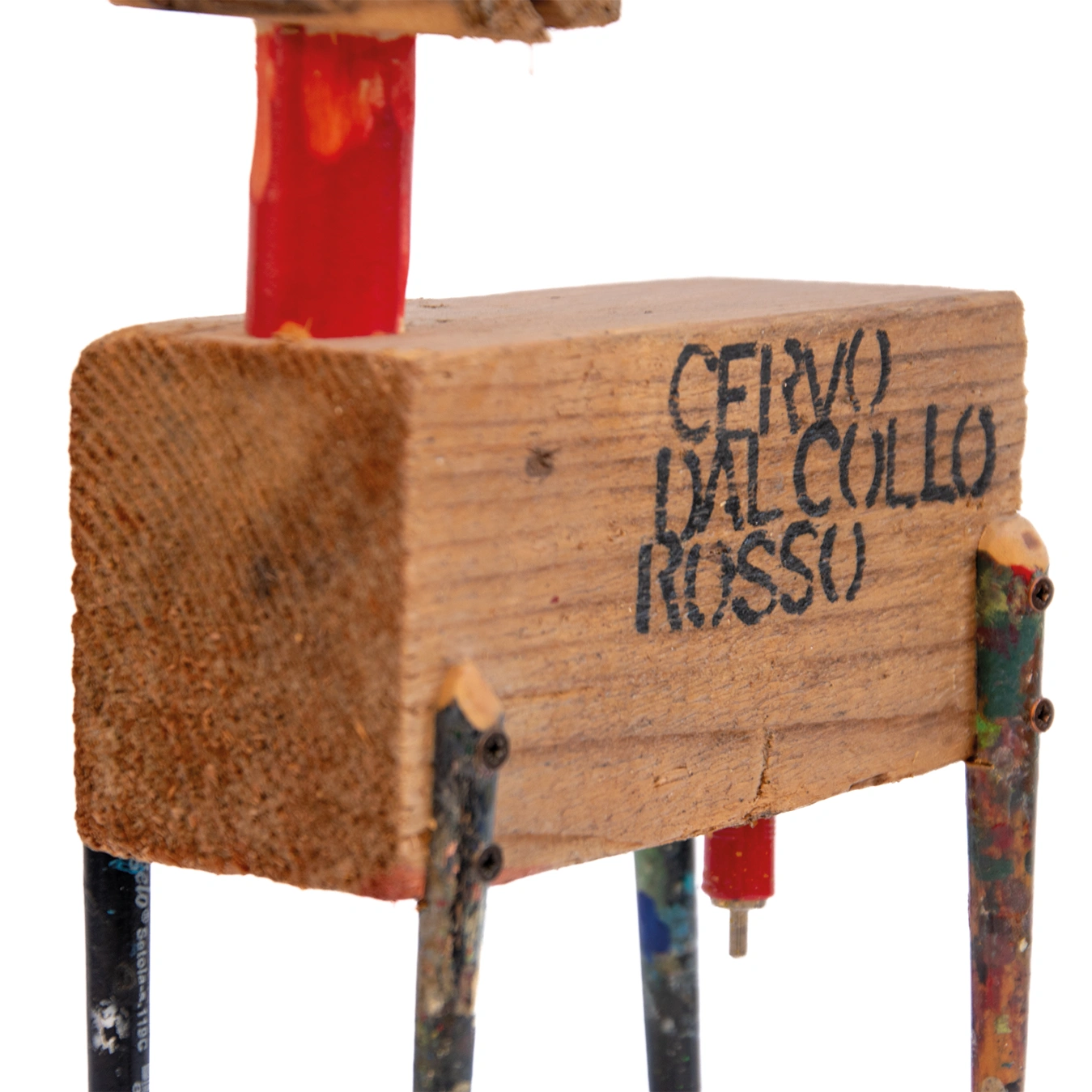 Un primo piano ravvicinato del blocco di legno centrale del cervo. Sul lato è chiaramente visibile il titolo stampigliato a caratteri neri "CERVO DAL COLLO ROSSO". In alto si nota la base del collo rosso verniciato. In basso sono visibili i punti di fissaggio delle zampe-pennello e un piccolo connettore elettrico rosso e metallico che pende dal ventre.