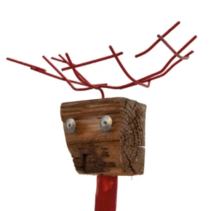 Un primo piano dettagliato della testa in legno della scultura. Due rondelle metalliche con viti al centro formano gli occhi dell'animale. Sopra il blocco di legno grezzo sono fissate le corna in metallo rosso ramificato. Sotto la testa si estende il collo in legno dipinto di rosso brillante.