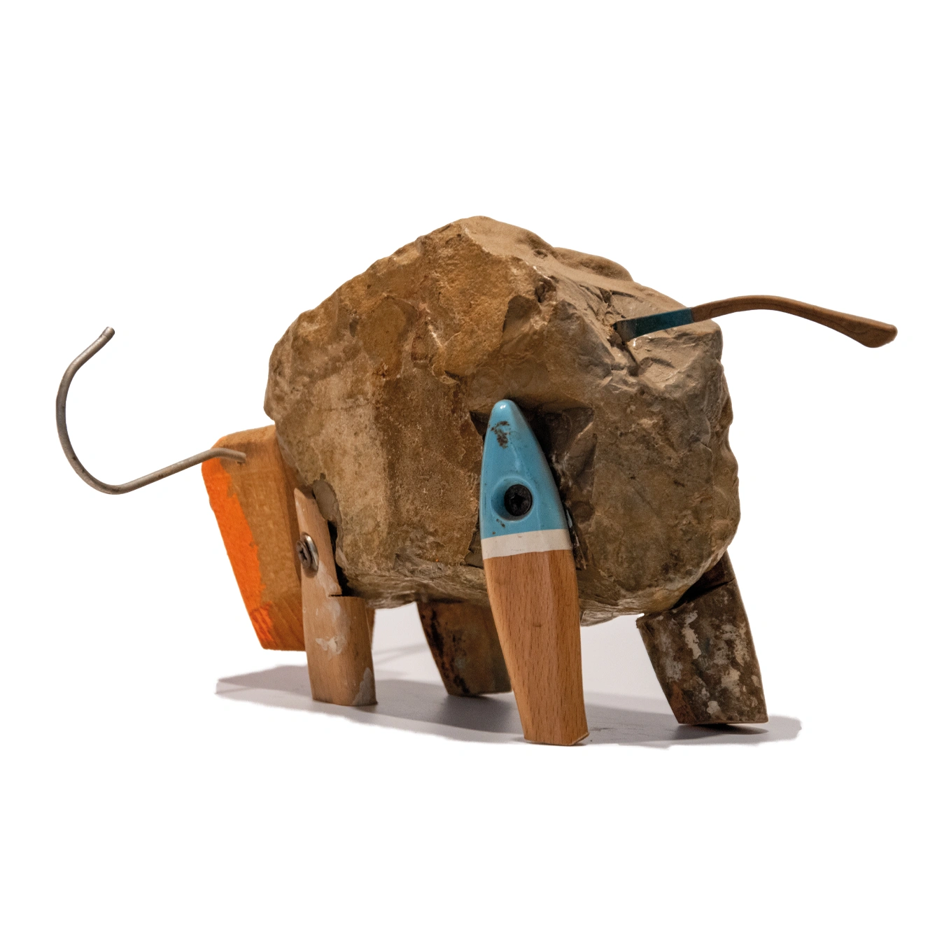 La parte posteriore di una scultura di toro stilizzato realizzata con una grande pietra naturale come corpo, gambe di legno grezzo e una coda in filo metallico curvato. Il corpo in pietra presenta la scritta a mano "TORO CLARO" in lettere scure. La scultura è del 2015.