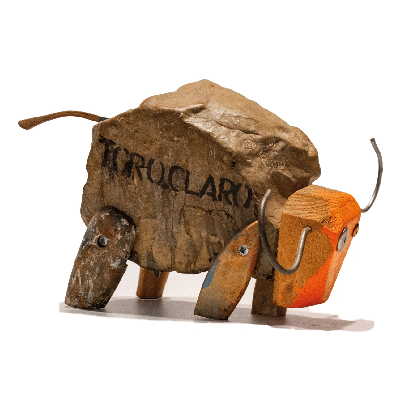 Una scultura "toro claro" raffigurante un toro stilizzato, creata assemblando una grande pietra naturale per il corpo, zampe di legno di recupero, una testa di legno dipinta di arancione acceso con un occhio a cerchio metallico, e fili metallici curvati per le corna e la coda. La scultura è del 2015.