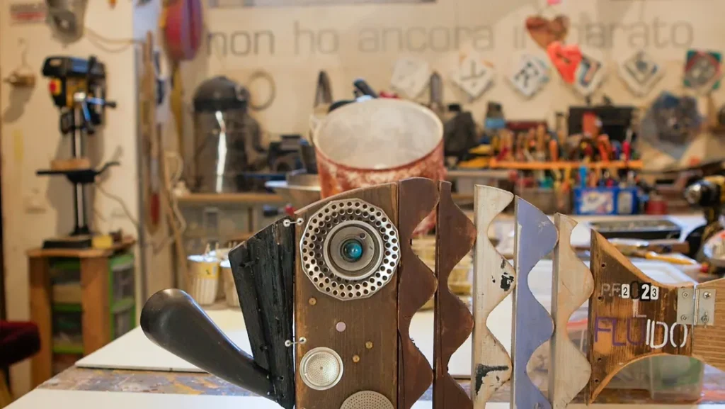bancone-da-lavoro-con-opera Primo piano di una scultura di pesce in legno e metallo intitolata "Il Fluido" sul bancone di lavoro di un laboratorio artigianale.