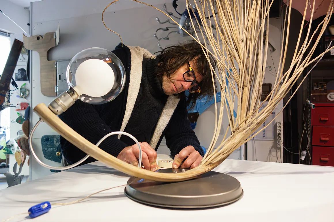 stefano-a-lavoro-lampada L'artista Stefano Pilato al lavoro nel suo laboratorio mentre assembla una lampada scultura in legno di recupero e rami.