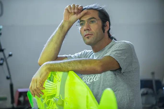 stefano-pilato-2015 L'artista Stefano Pilato in posa sotto una grande scultura metallica a forma di navicella o modulo spaziale installata su un prato