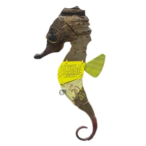 Scultura a parete in legno e metallo raffigurante un cavalluccio marino con occhiali e la scritta L'AMANTE DI CRUCIVERBA A SCHEMA LIBERO"