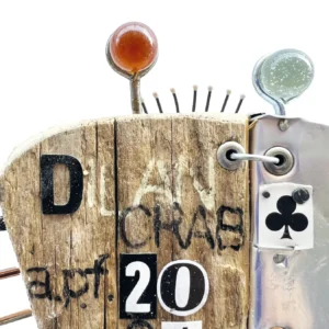 Dettaglio del corpo della scultura Dilan Crab in legno con etichetta di carta da gioco asso di fiori, occhi in vetro e la scritta DILAN CRAB APF 2026